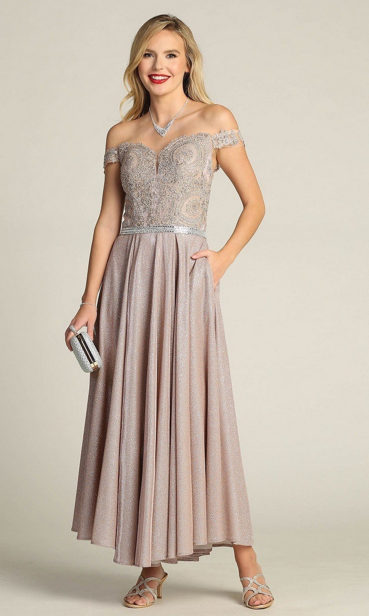 A woman stands against a plain background wearing the Chicas DM4027 Tea-Length Formal Dress in rose, featuring off-the-shoulder styling, delicate lace detailing, and a shimmering A-line skirt. She holds a silver clutch in her hand.